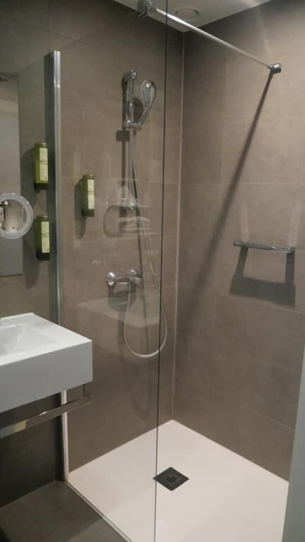 Una ducha moderna con puerta de vidrio, un lavabo blanco y un espejo.