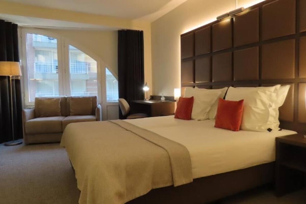 A hotel room with a large bed, a sofa, a desk, and a window with curtains.