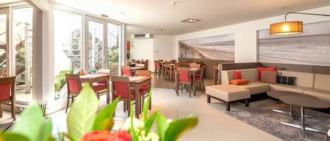 Un moderno vestíbulo de hotel con comedor, un sofá y un amplio ventanal con vistas a un jardín.