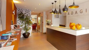 A reception desk with a glass top, a potted plant, and a wall-mounted sign reading "ADAGIO". - Adagio hotel (Knokke-Heist)