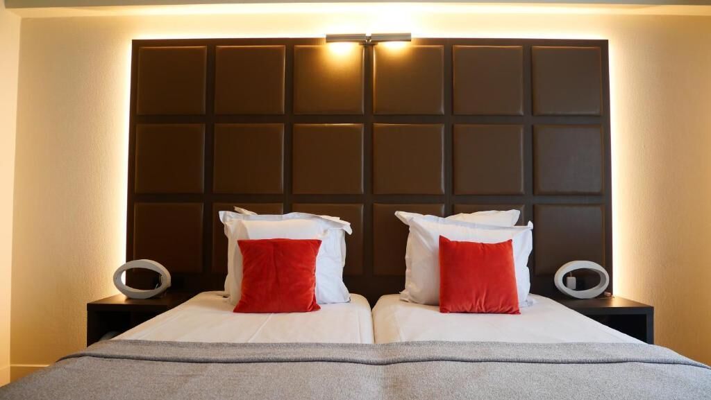 Un lit double avec une tête de lit, deux tables de chevet et des oreillers rouges et blancs.