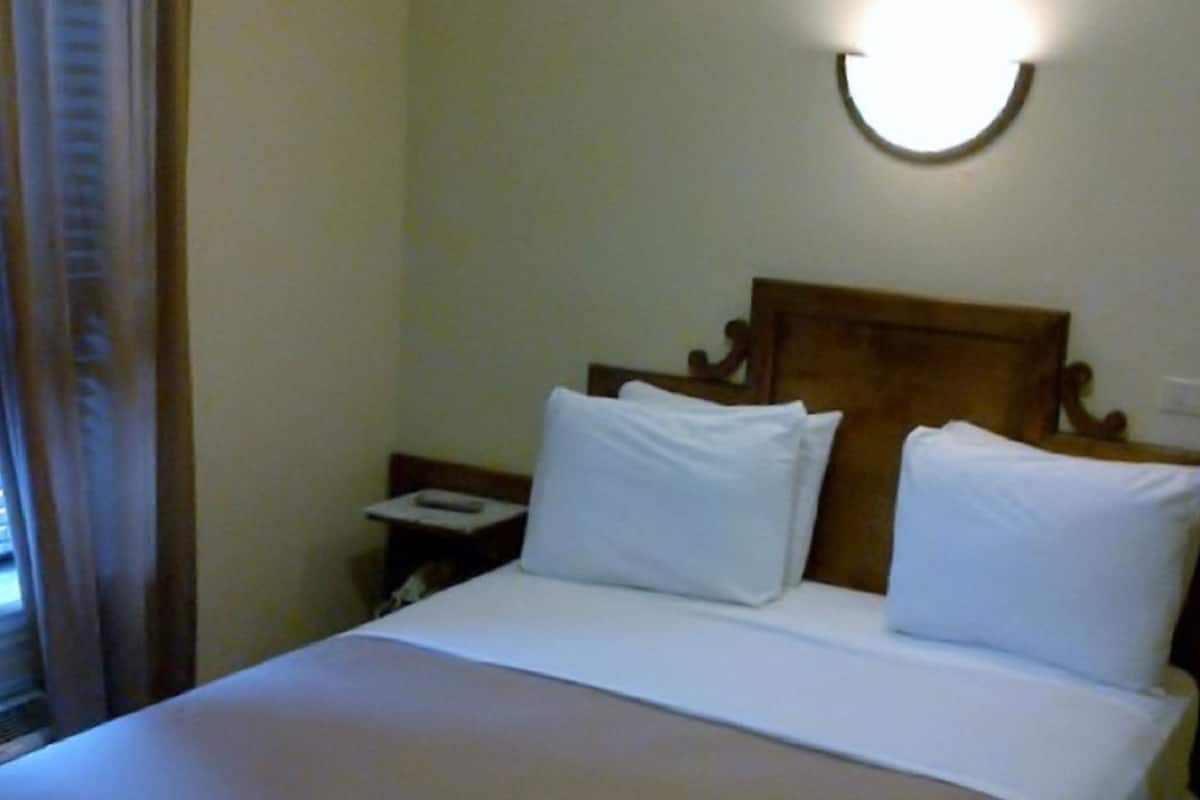 Una habitación de hotel con una cama grande, una mesita de noche y una lámpara fijada a la pared.