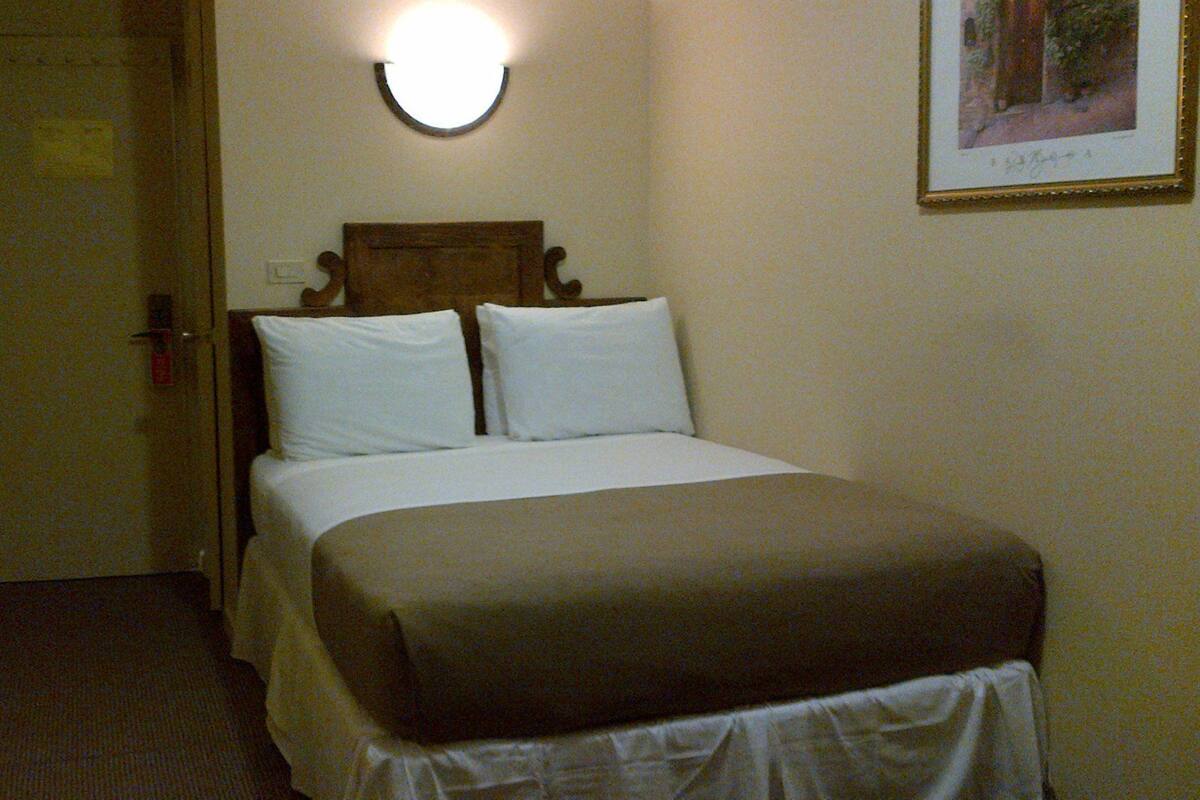 Una habitación de hotel con una cama, una puerta y una lámpara fijada a la pared.