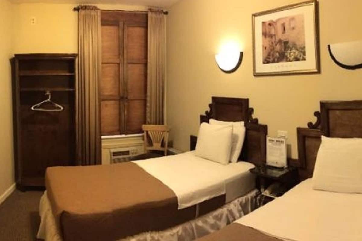 Una habitación de hotel con dos camas, un armario, una televisión y una ventana con cortinas.