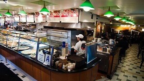 A food counter with a chef preparing food, a menu board, and a variety of food items displayed. - St Marks Hotel (New York)