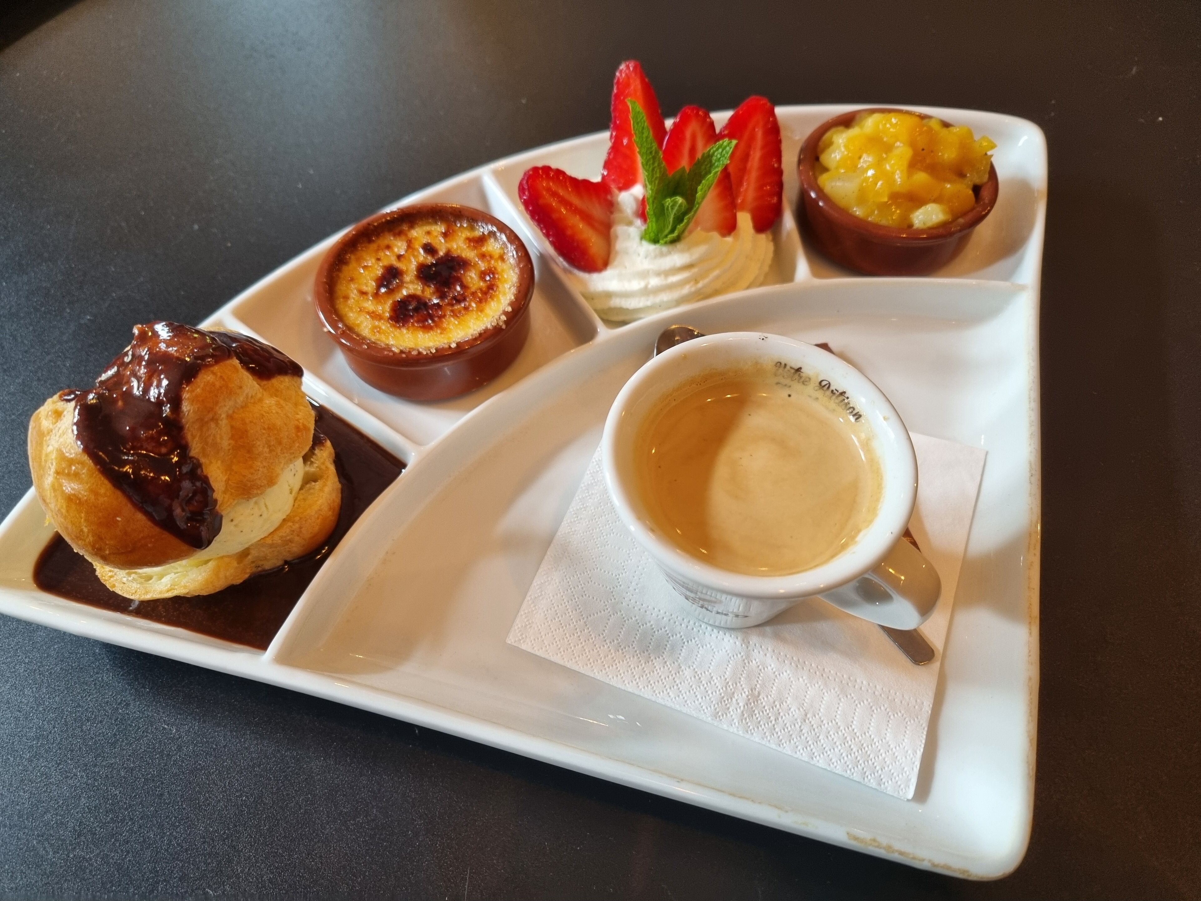 Un plateau avec une crêpe, une crème dessert, une salade de fruits et une tasse de café.