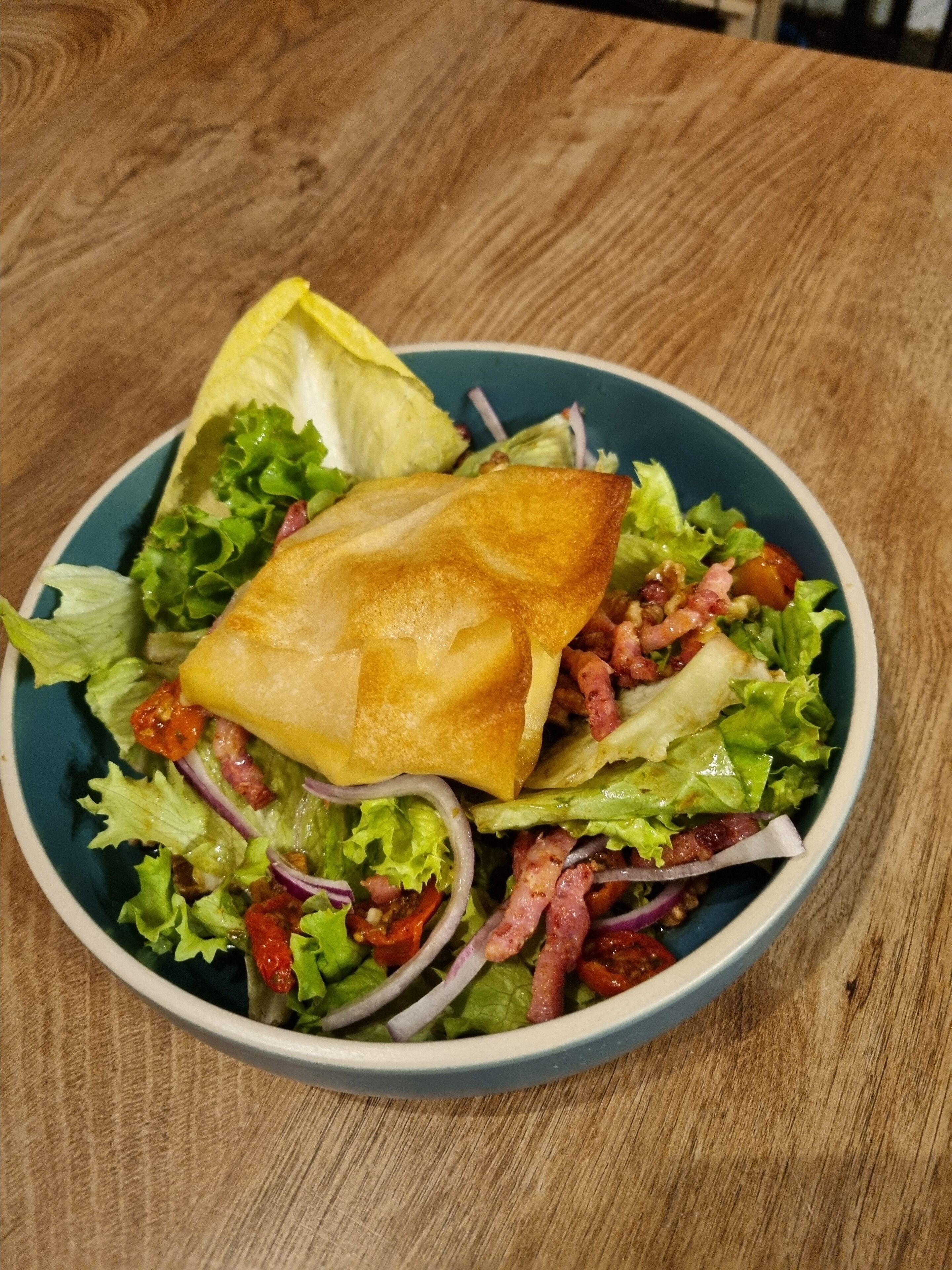 A bowl of salad with lettuce, tomatoes, and red onions on a wooden table.