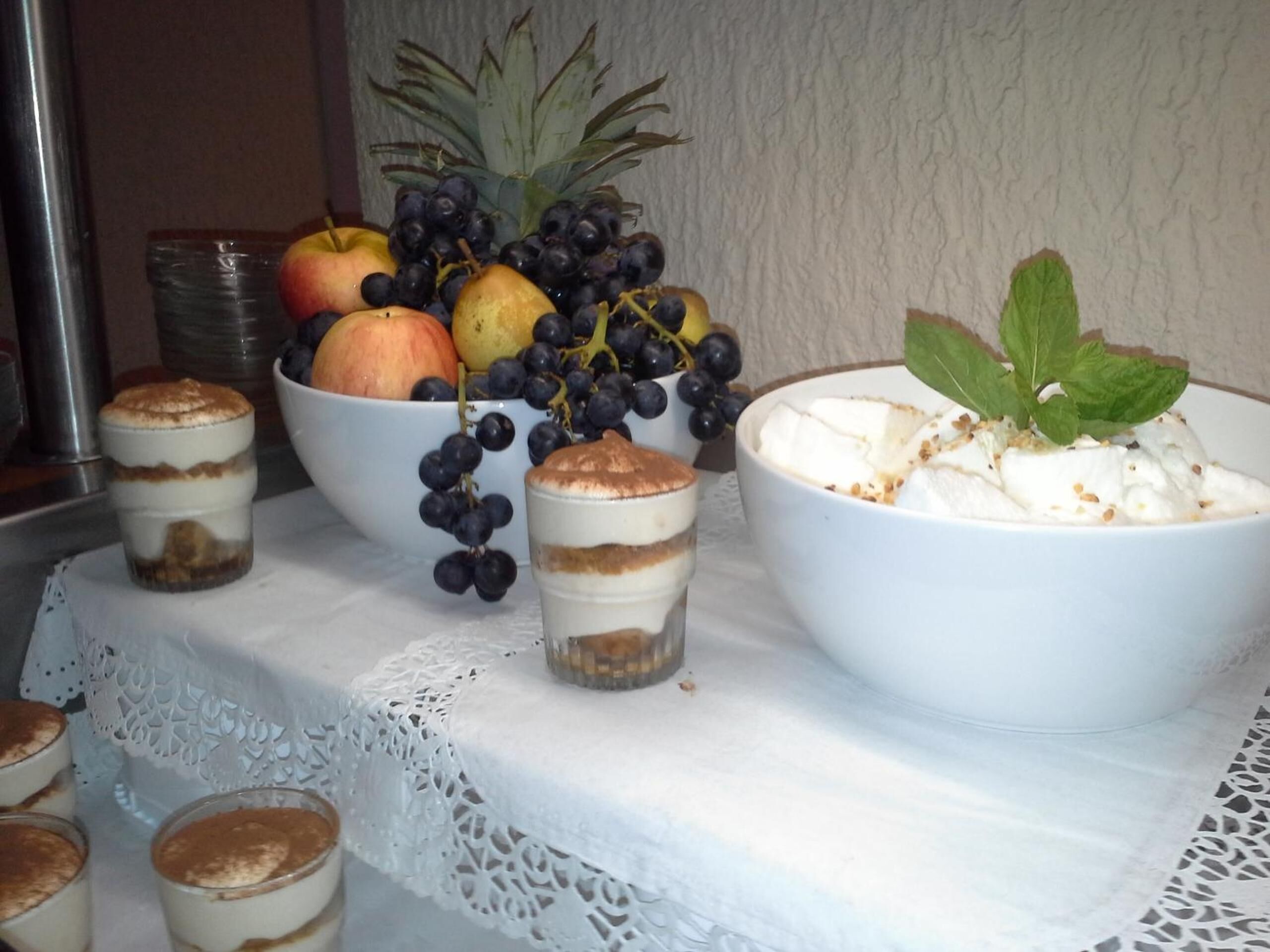 A dessert table with layered desserts, a bowl of fruit, and a decorative plant.