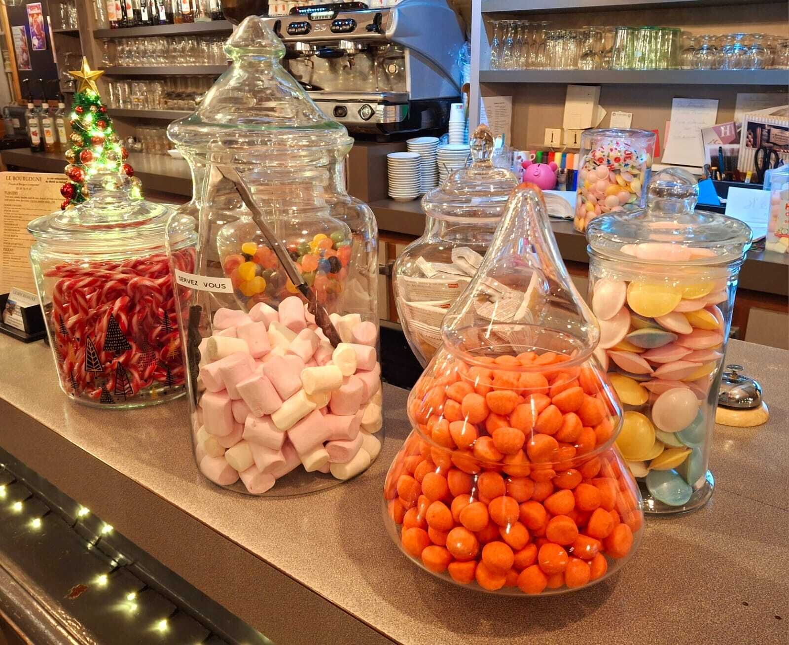 Diversos potes de doces em um balcão, incluindo marshmallows, balas de goma e guloseimas coloridas.