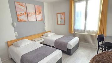 A hotel room with two beds, a small table, a chair, and a window with curtains.