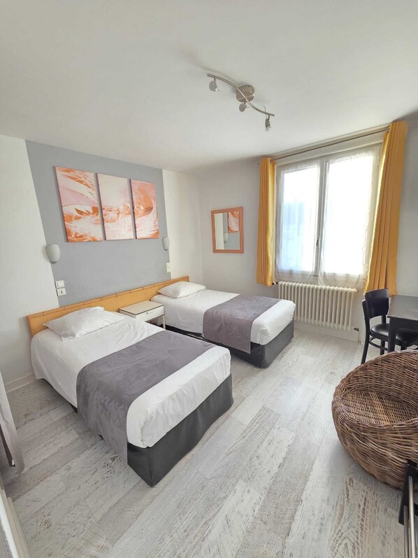 A hotel room with two beds, a small table, a chair, and a window with curtains.