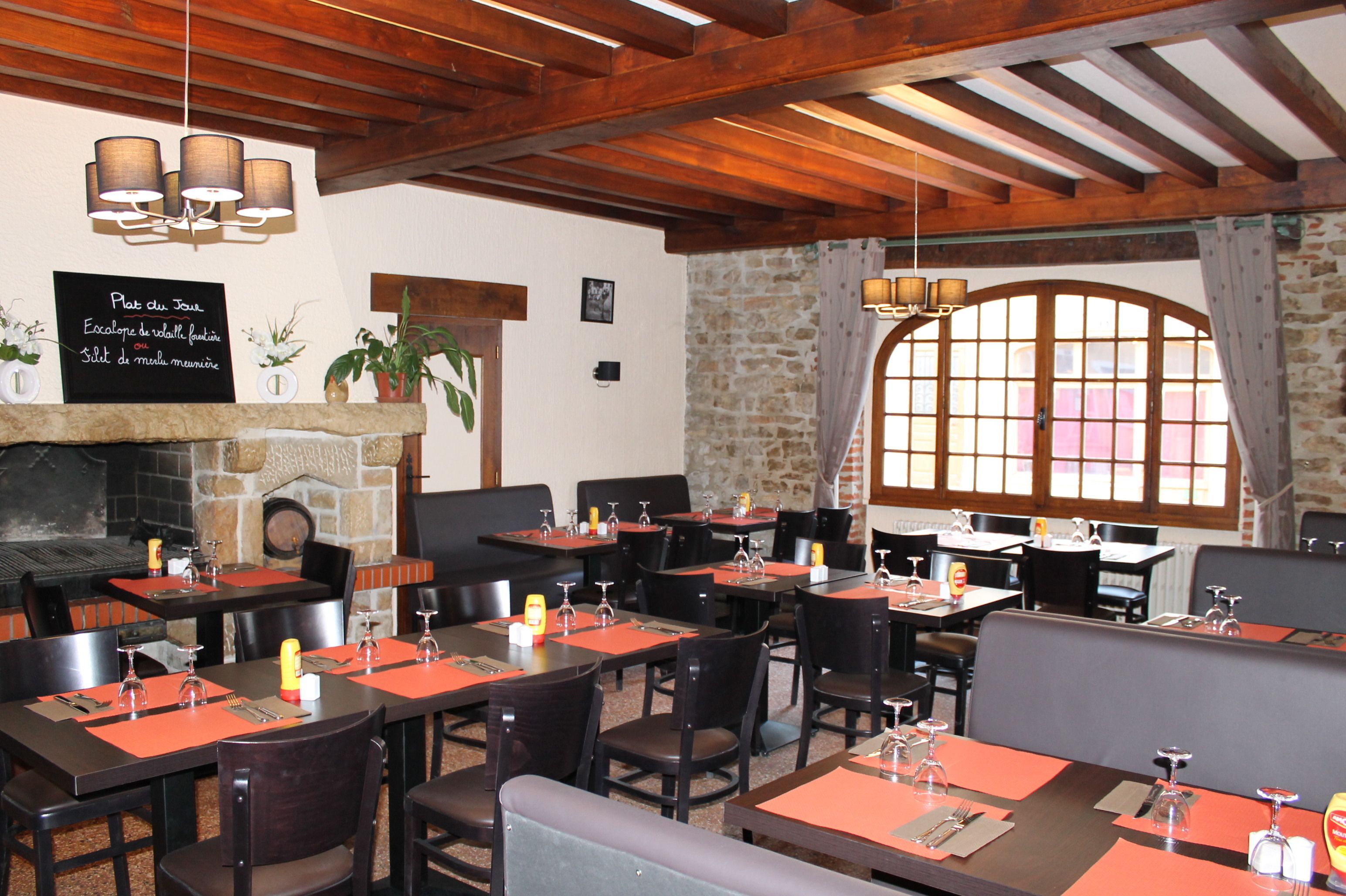 A restaurant with wooden beams, stone walls, and large windows. Tables are set with red placemats and wine glasses.