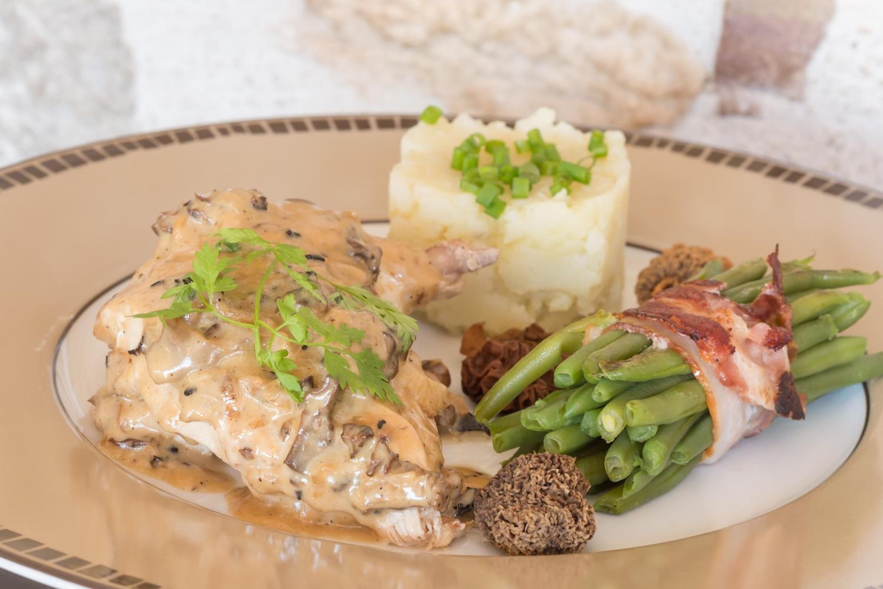 Une assiette composée de poulet, de purée de pommes de terre, de haricots verts et d’un plat aux champignons.