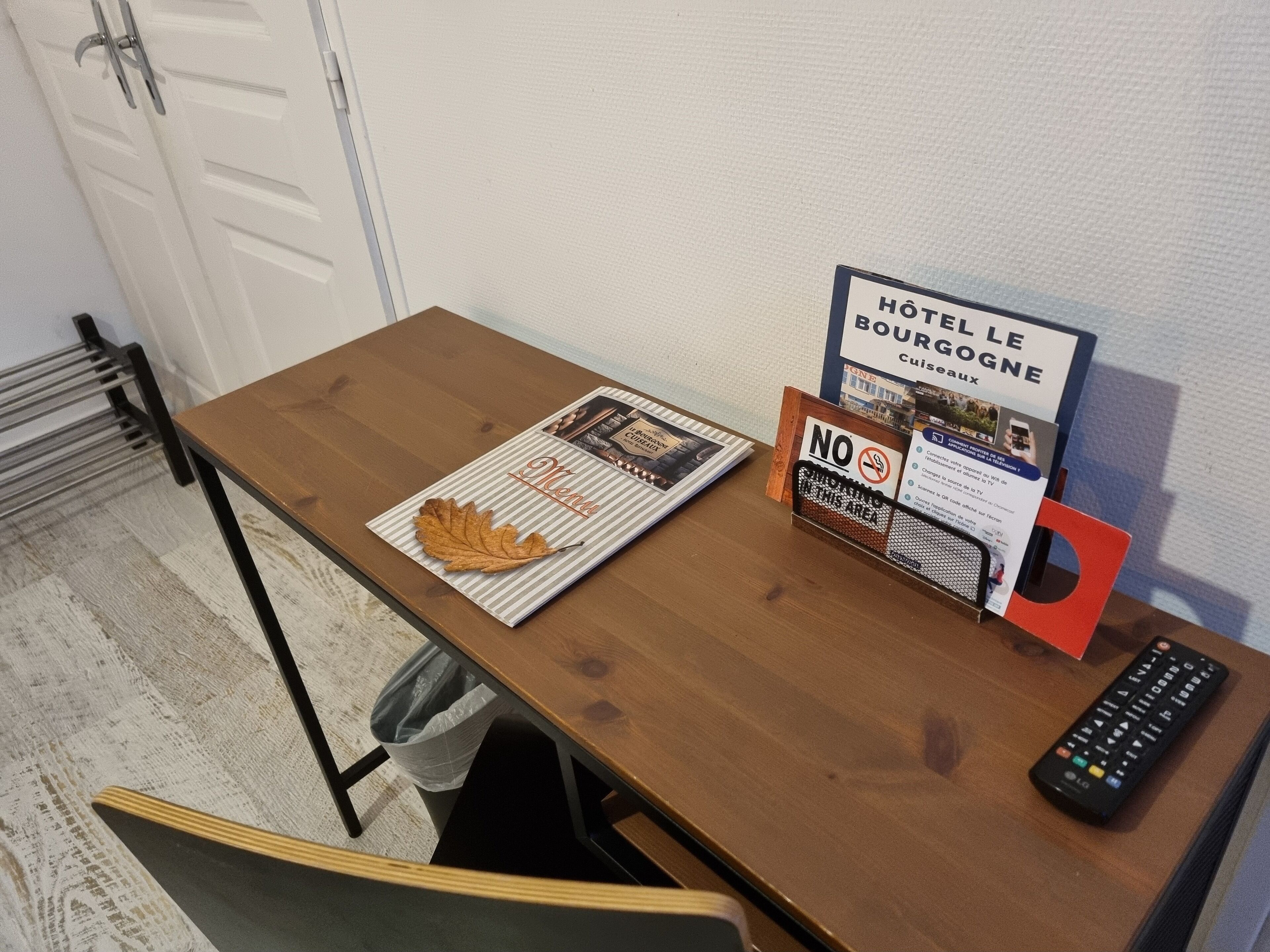 Ein Holztisch mit einer Zeitschrift, einem Rauchverbotsschild, einer Fernbedienung und einem kleinen Mülleimer.