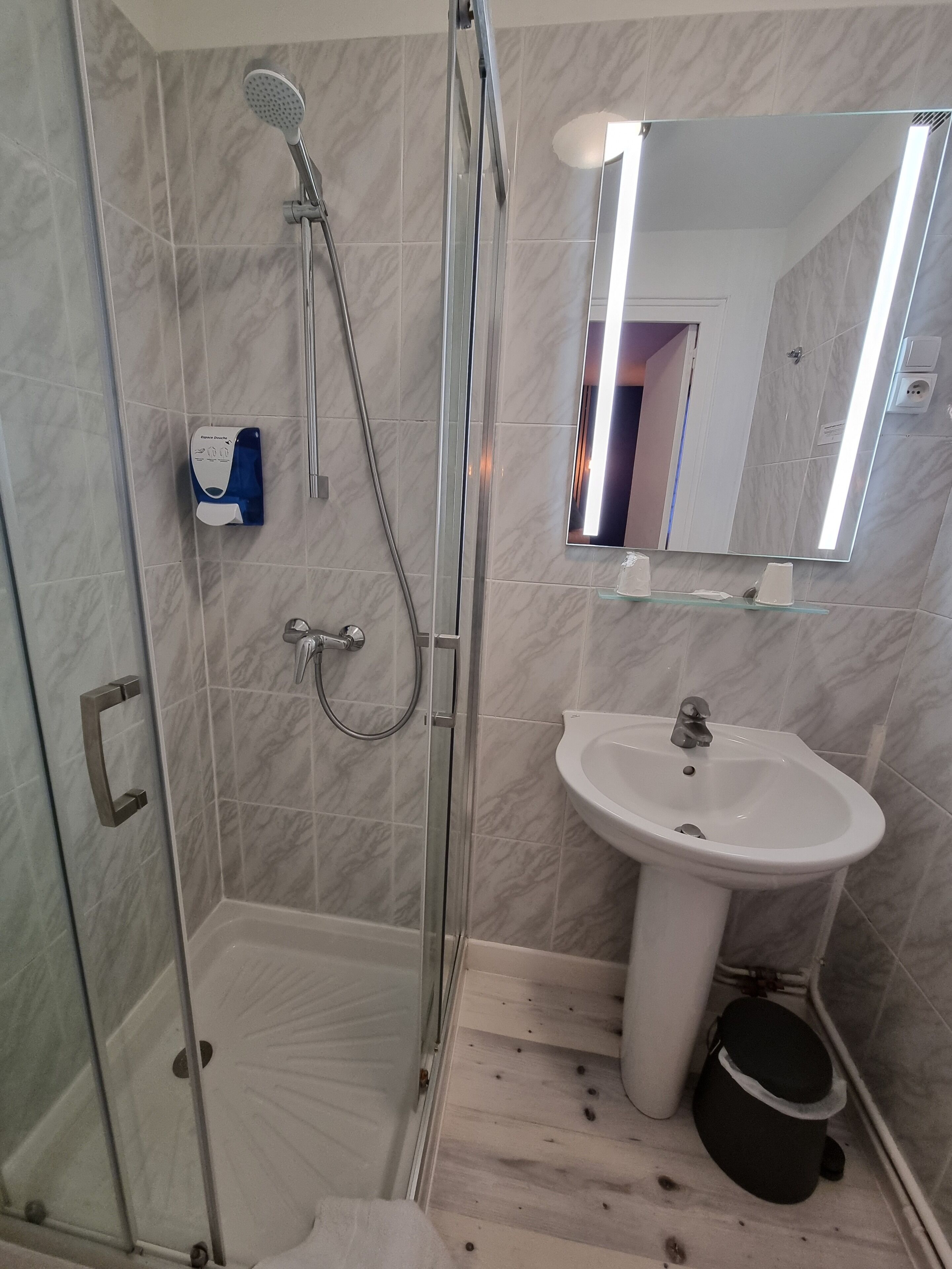 Un baño con ducha envuelta en vidrio, lavamanos sobre pedestal y espejo encima.