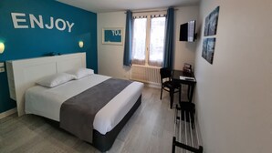 Een hotelkamer met een bed, een bureau, een stoel, een radiator en een raam met gordijnen.