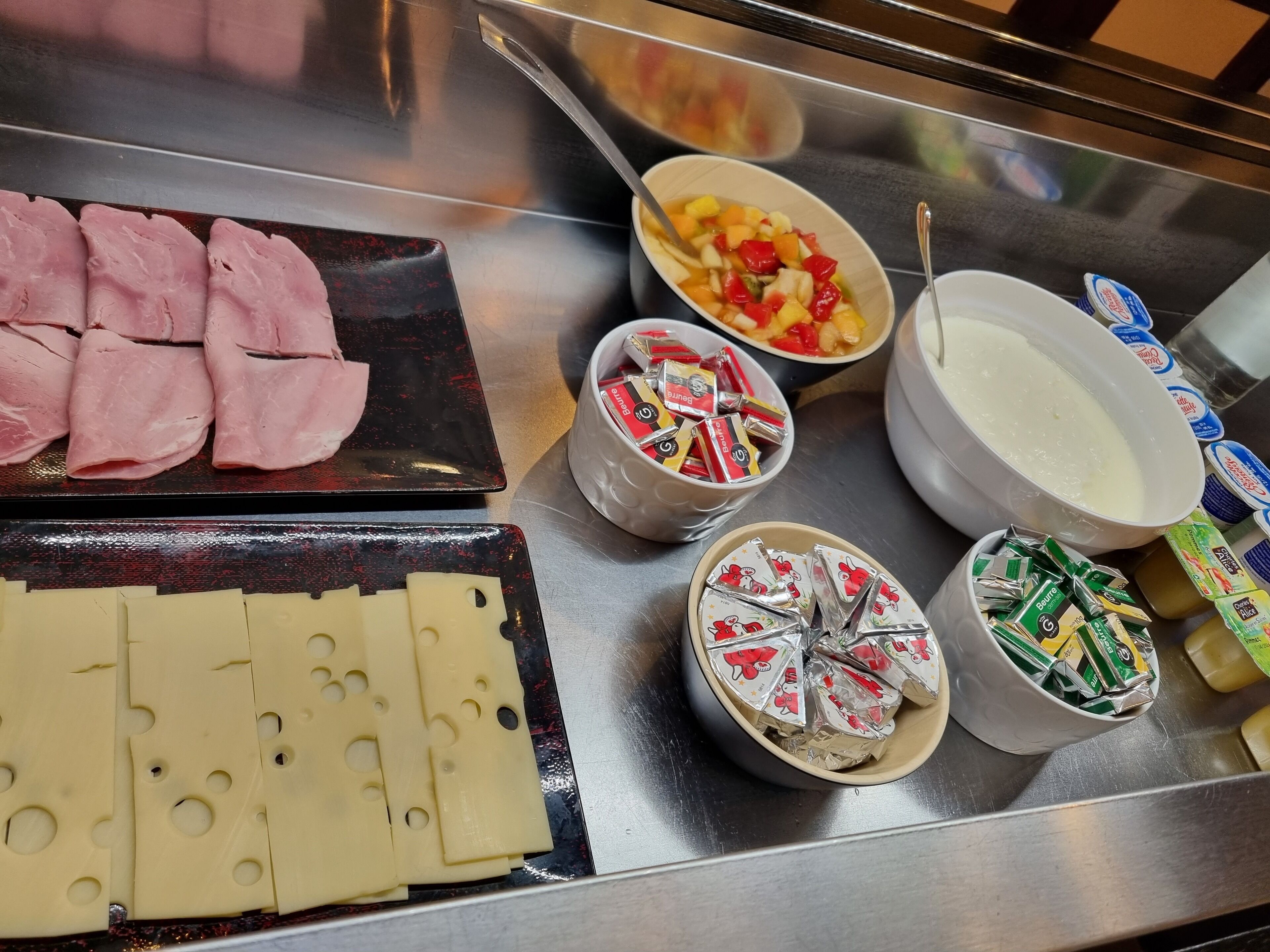 A variety of food items including sliced ham, cheese, and packaged snacks on a stainless steel counter.