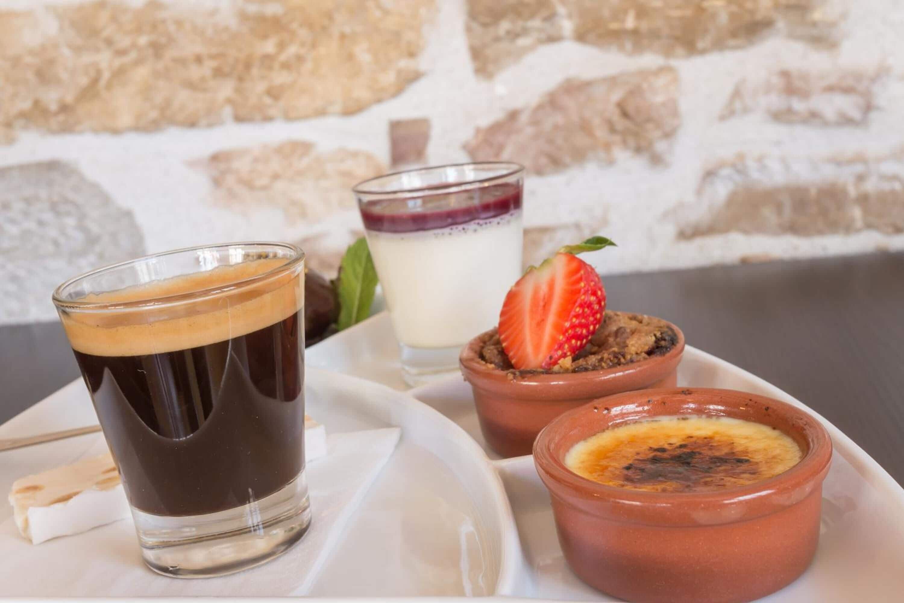 Un plateau de desserts avec un verre contenant un liquide sombre, probablement du café, et deux petits récipients contenant des desserts garnis de fraises.