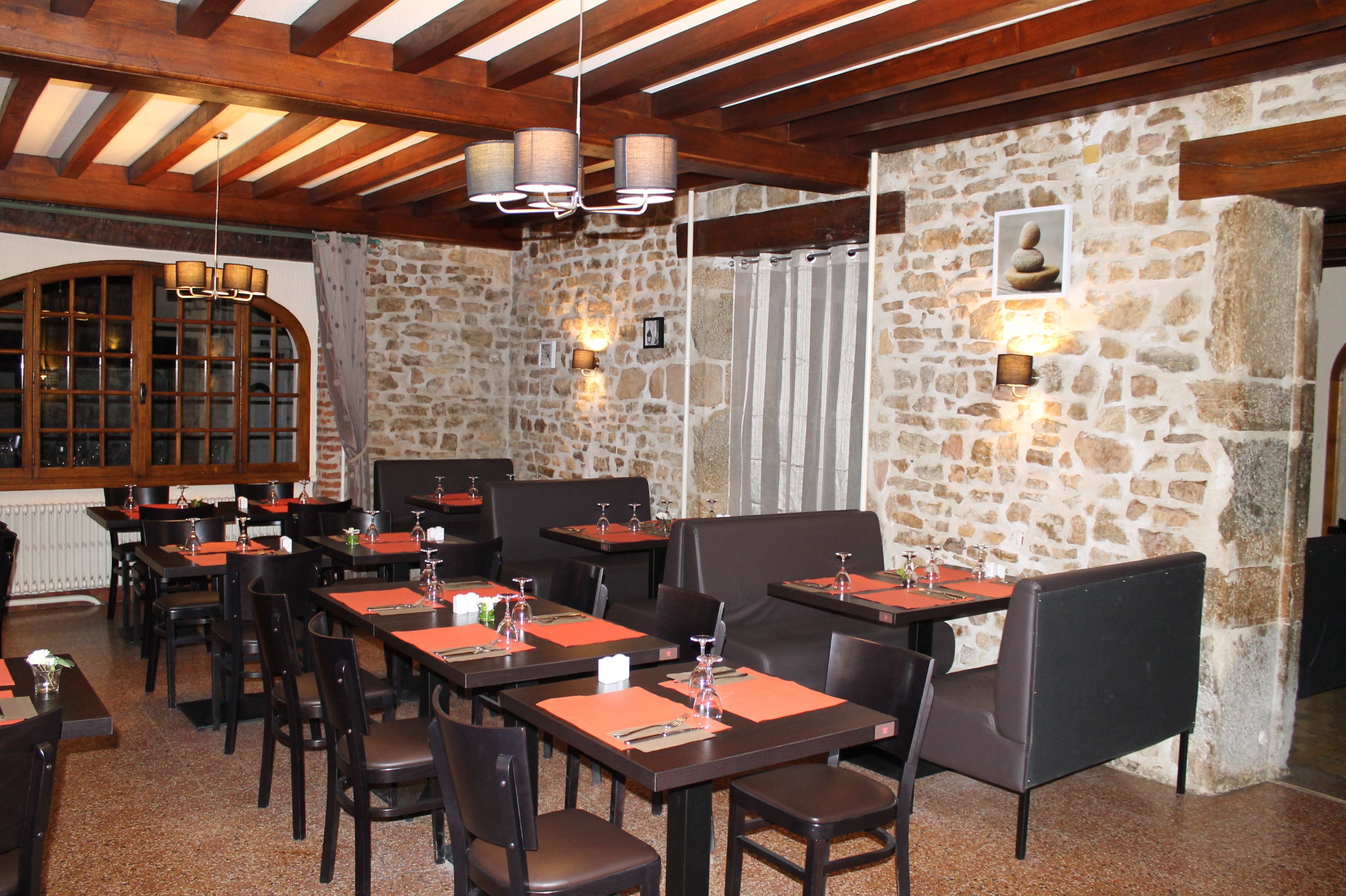 Un restaurant aux murs de pierre, aux poutres apparentes et doté de nombreuses tables accompagnées de chaises.