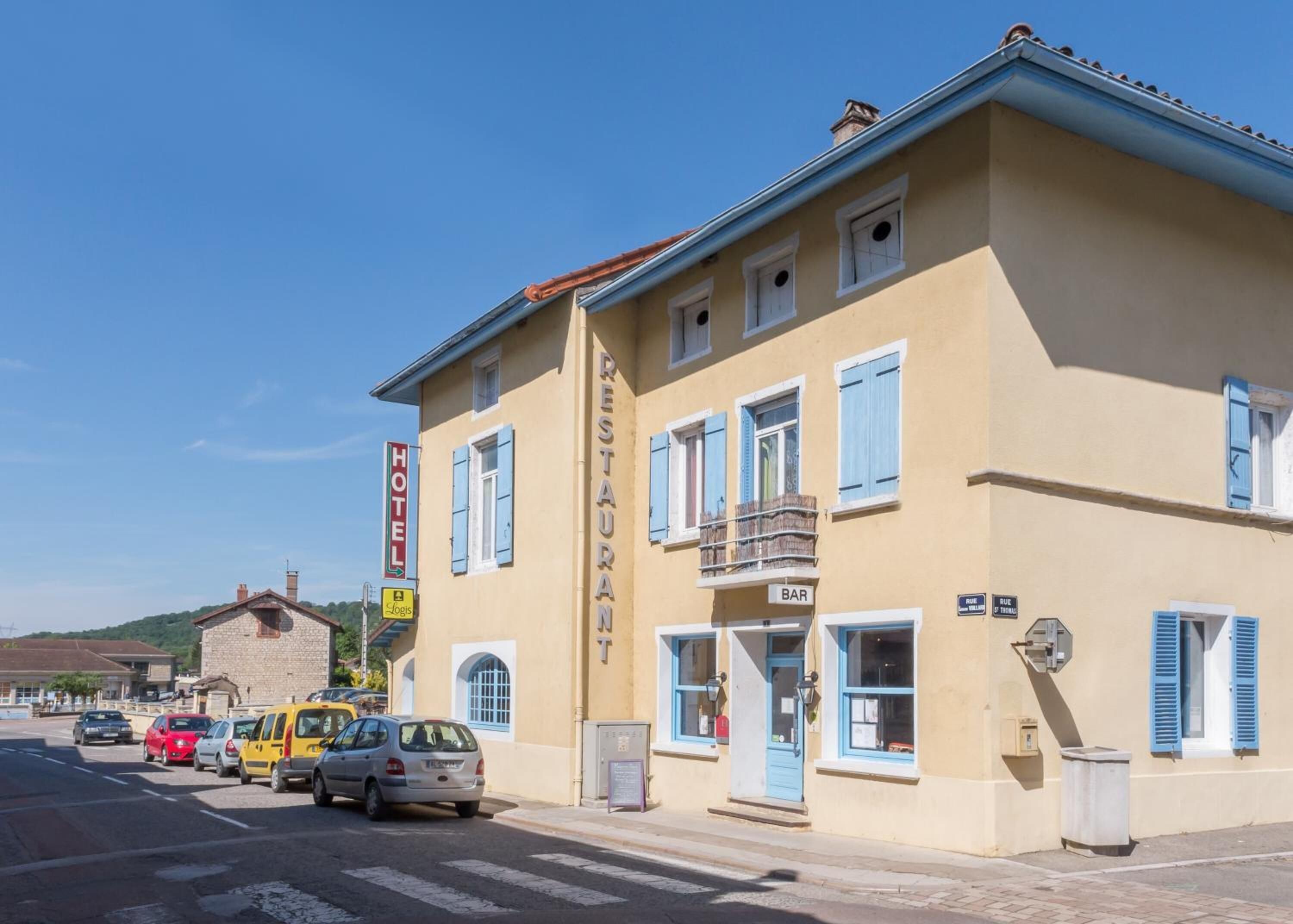 Um edifício de dois andares com uma placa indicando um hotel e um bar. Há carros estacionados em frente ao prédio.