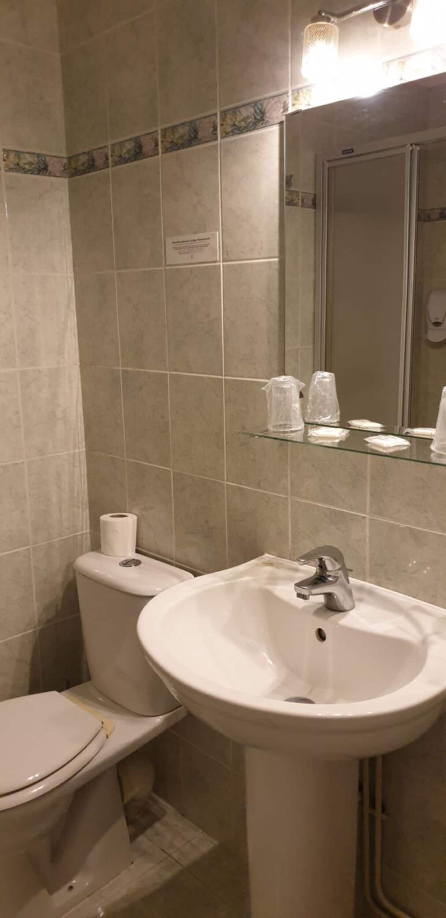 A bathroom with a toilet, sink, and mirror. There are toiletries on the sink's edge.