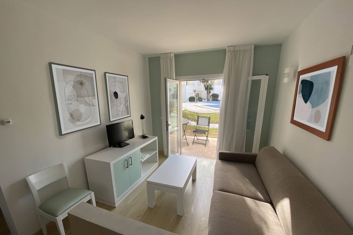 A living room with a sofa, a TV on a cabinet, a small table, and a bench.