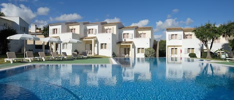 Una piscina al aire libre, sombrillas, sillones reclinables de piscina