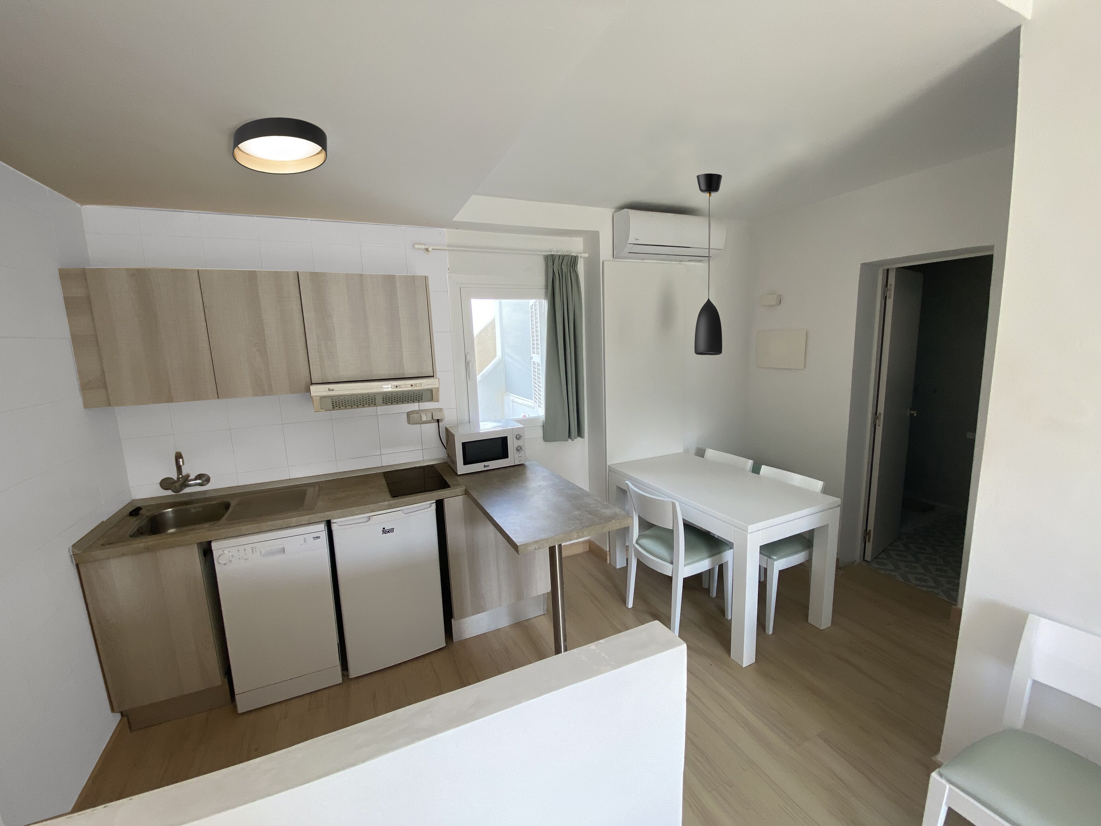 Una cocina moderna con lavavajillas, microondas y comedor con mesa y sillas.