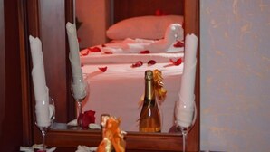 Une chambre à coucher avec un lit recouvert de pétales de roses, une bouteille de champagne et des bougies.