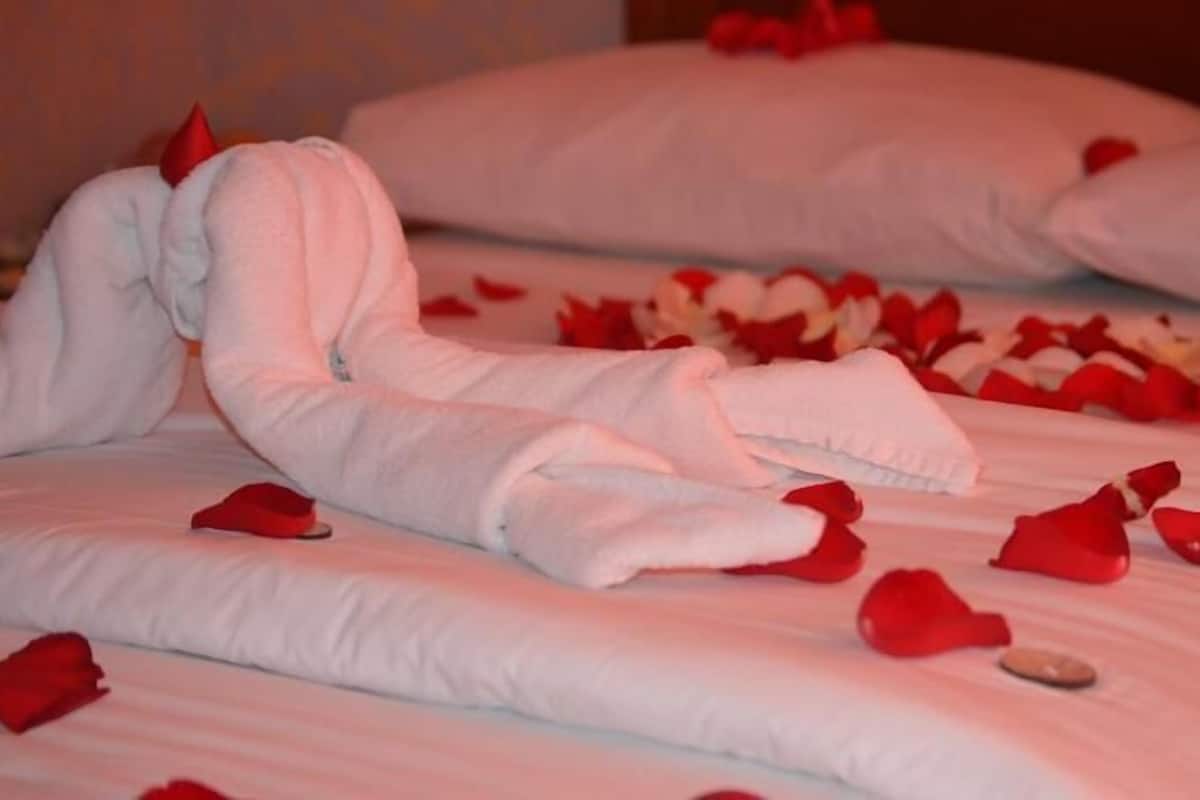 Un lit recouvert de draps blancs et parsemé de pétales de roses rouges.