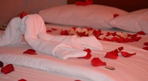 A bed with white linens and red rose petals scattered on it.