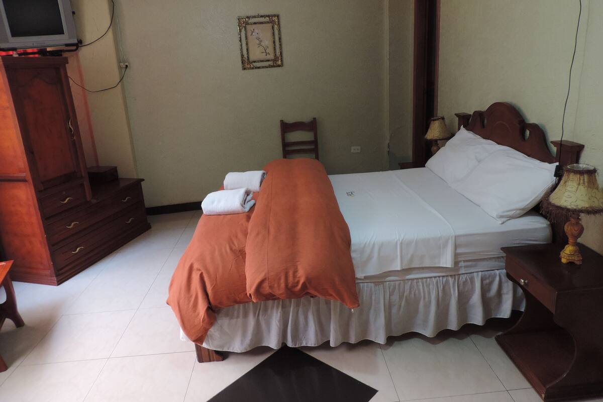 Une chambre d’hôtel avec un lit, une commode en bois, un téléviseur et une lampe.