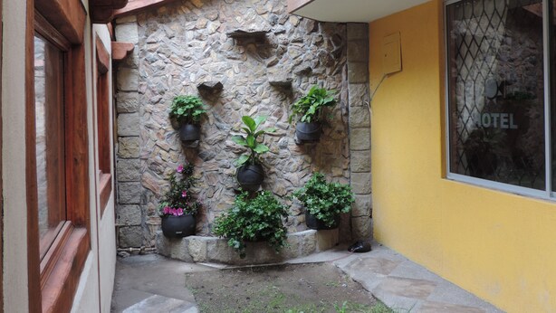 Un mur de pierre agrémenté de plantes en pot, une porte en bois et une fenêtre avec une grille en métal.