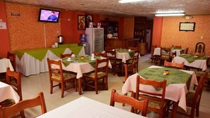 Un restaurant avec plusieurs tables et chaises, un téléviseur accroché au mur et un réfrigérateur au fond de la pièce.