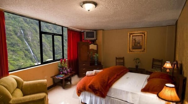 A bedroom with a bed, a chair, a desk, a dresser, and a window with a view of a waterfall.