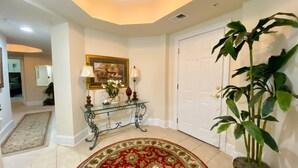 A hallway with a glass console table, a red and gold patterned rug, a potted plant, and a door. - Barefoot Resort by Palmetto Vacations (North Myrtle Beach)