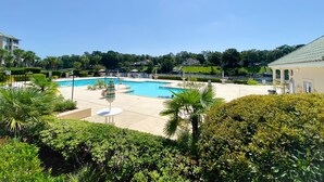A large outdoor swimming pool surrounded by lush greenery and palm trees, with a clear blue sky above. - Barefoot Resort by Palmetto Vacations (North Myrtle Beach)