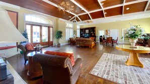 A spacious lobby with wooden flooring, a high ceiling with exposed beams, a chandelier, and a large table with a vase of flowers. - Barefoot Resort by Palmetto Vacations (North Myrtle Beach)