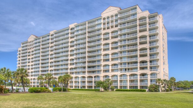A large, multi-story hotel with numerous balconies and a well-maintained lawn in front. - Barefoot Resort by Palmetto Vacations (North Myrtle Beach)