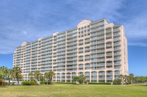Un hotel grande de varios pisos con numerosos balcones y un césped bien cuidado al frente.
