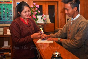 A reception desk with a wooden counter, a bell, and a poster of birds of Myanmar. - Shwe Inn Tha Floating Resort Hotel (Nyaungshwe)