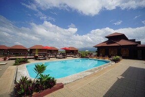 A swimming pool with lounge chairs and umbrellas, surrounded by potted plants and a building with a tiled roof. - Shwe Inn Tha Floating Resort Hotel (Nyaungshwe)