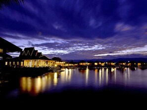 A waterfront hotel with a prominent building featuring a triangular roof and a well-lit entrance. - Shwe Inn Tha Floating Resort Hotel (Nyaungshwe)