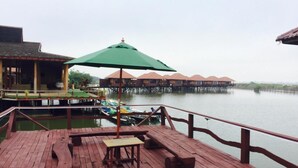 A wooden deck with a bench and a table, overlooking a calm body of water with overwater bungalows in the background. - Shwe Inn Tha Floating Resort Hotel (Nyaungshwe)