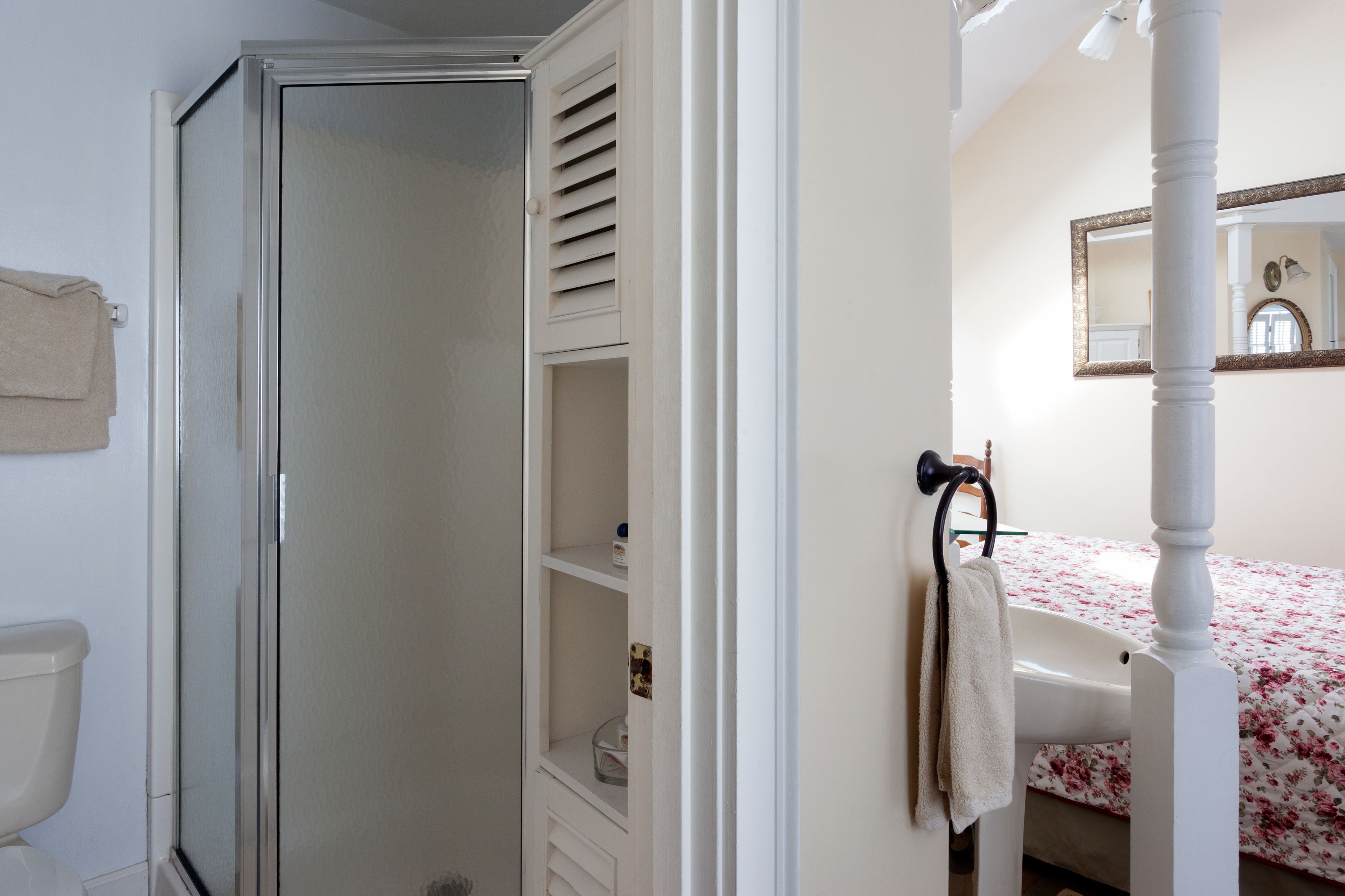 Une salle de bain avec douche, toilettes et un lit recouvert d’une couvre-lit à motifs floraux.