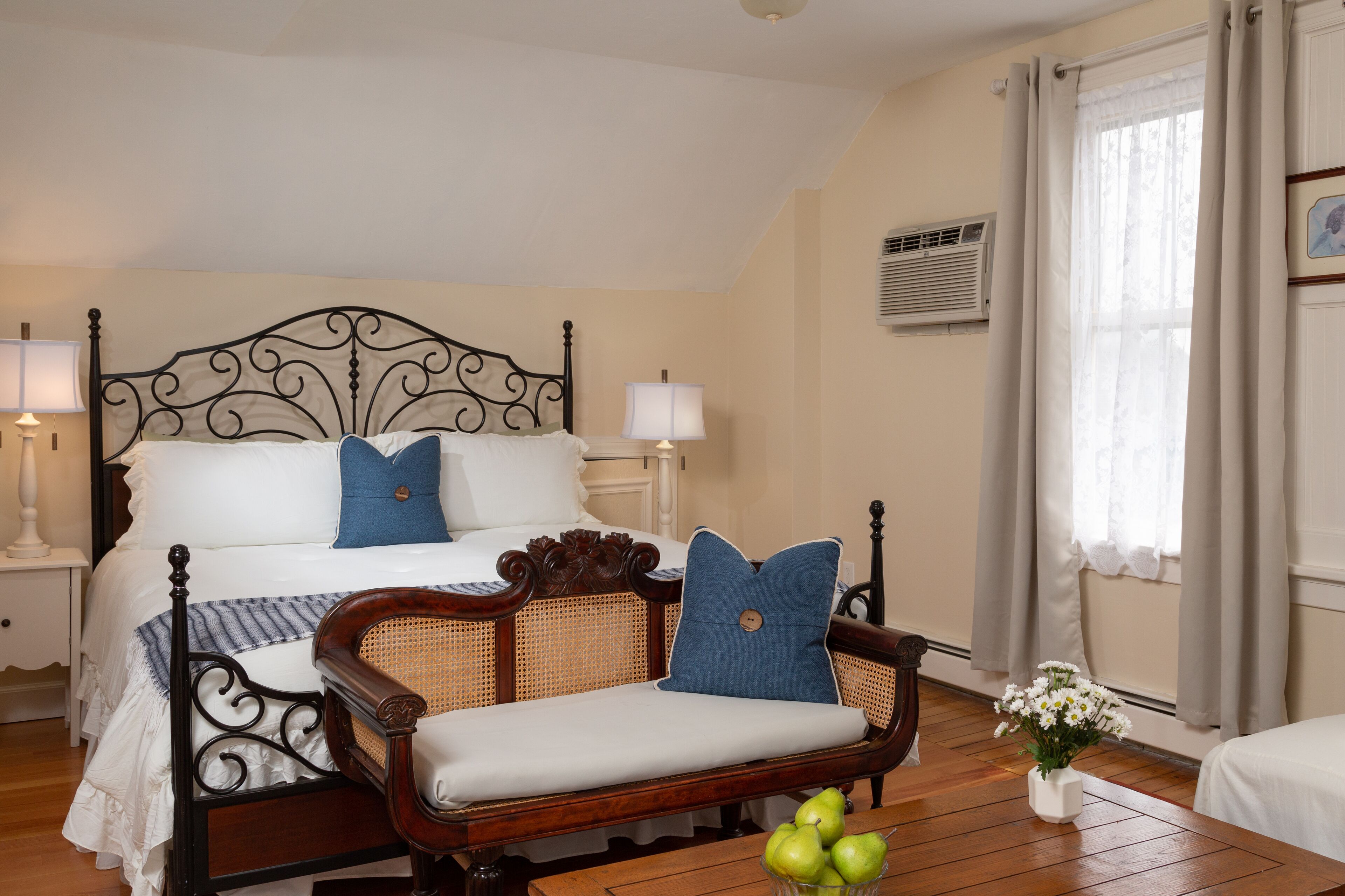 A bedroom with a four-poster bed, a wooden bench, and a bedside table with a lamp.