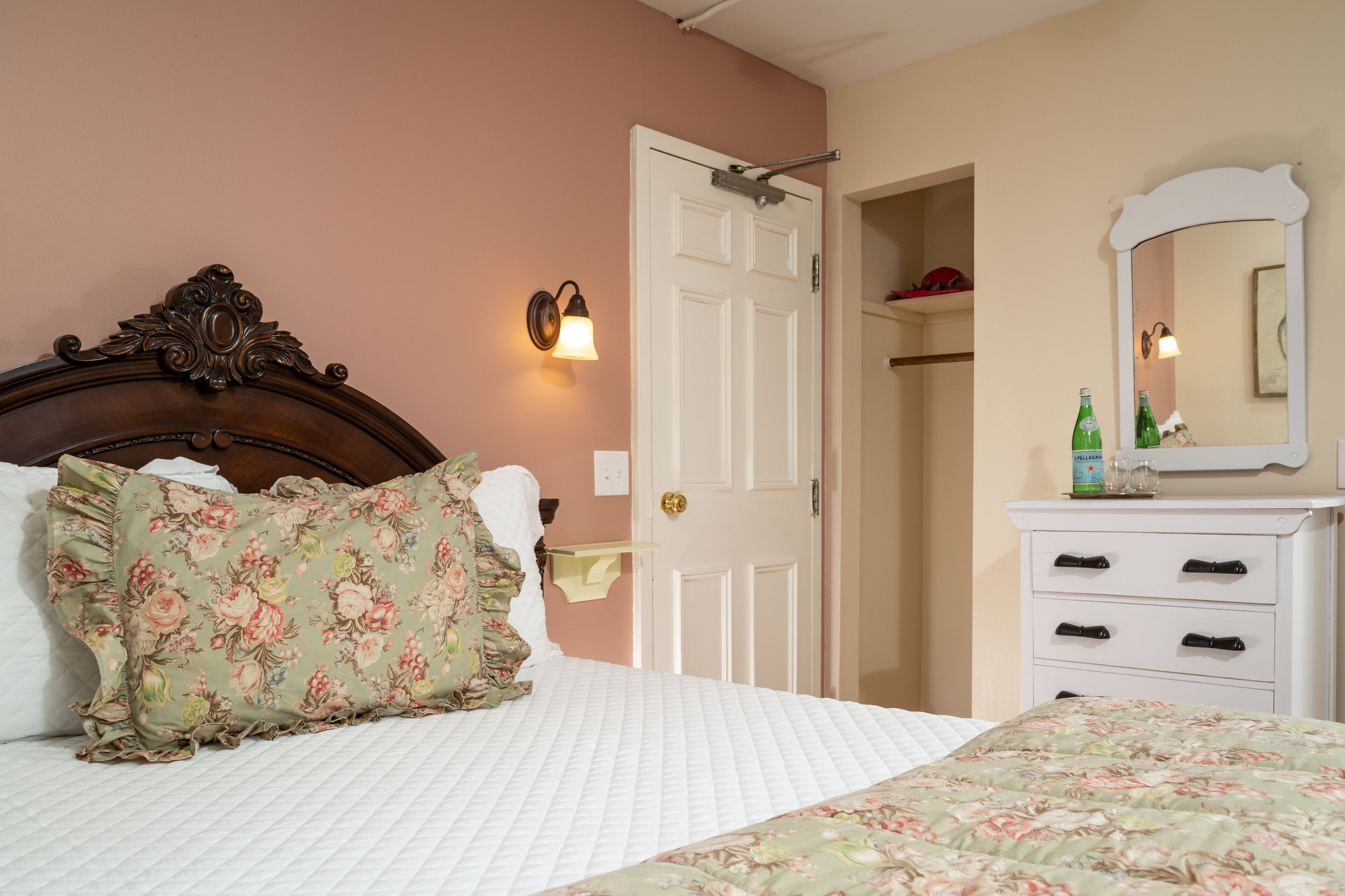 A bedroom with a bed, a dresser, a door, and a mirror.