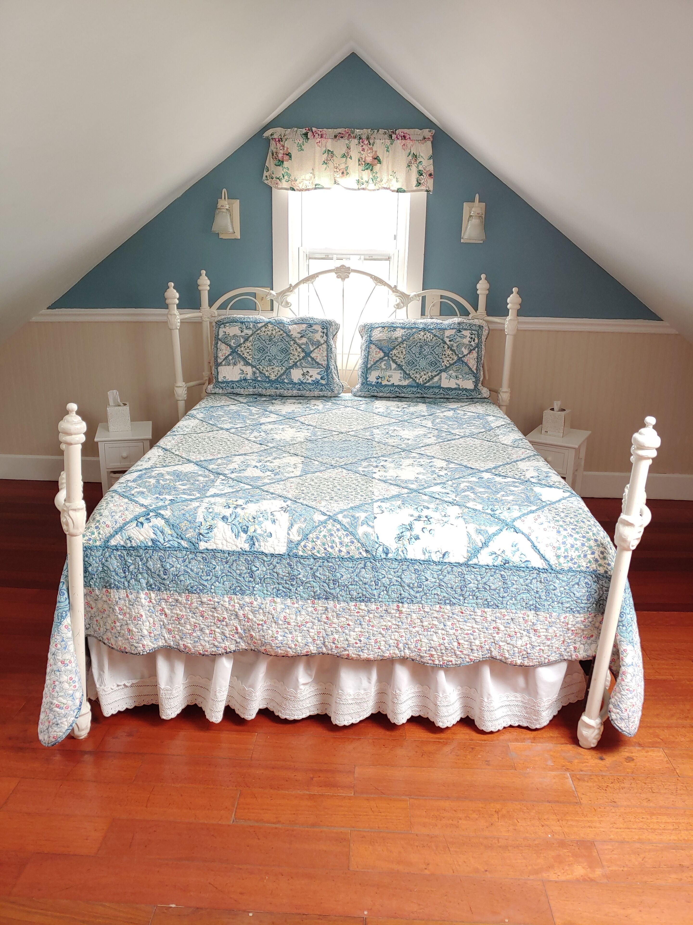 Un dormitorio con cama, cabecera blanca y ventana con adornos florales.