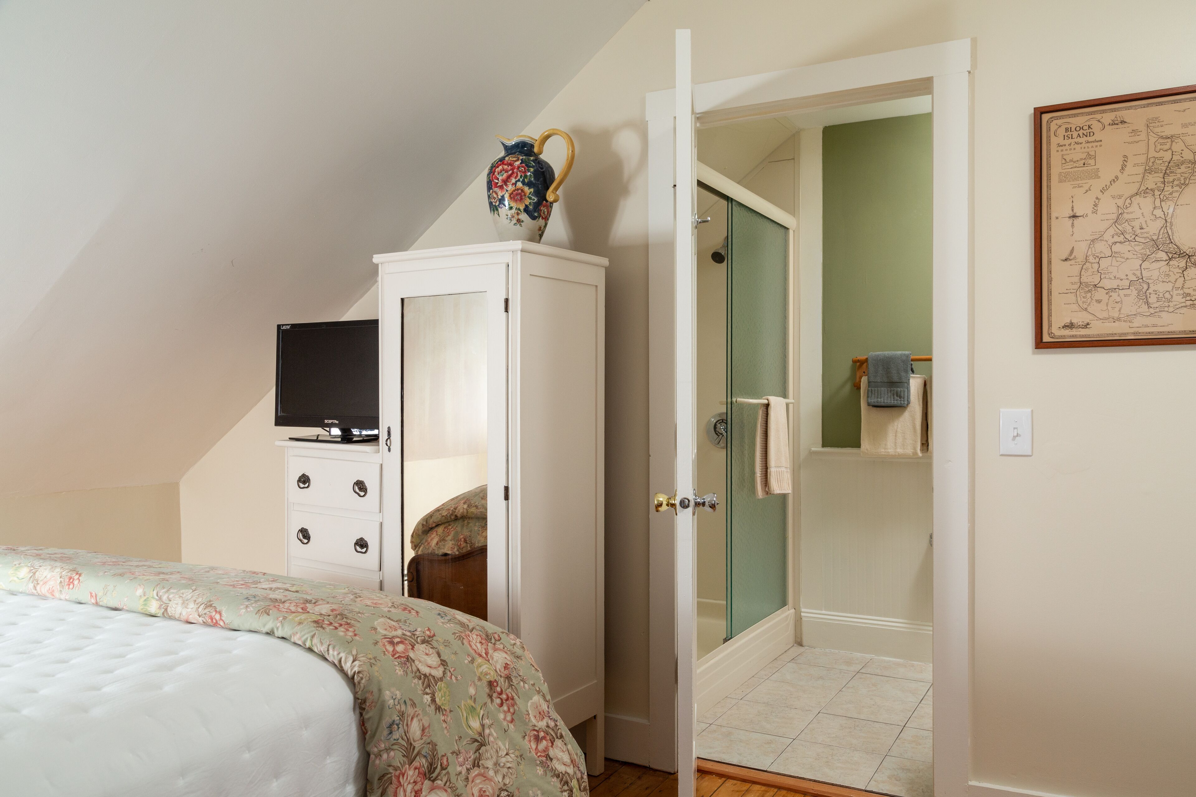 Un dormitorio con cama, armario, televisor y baño con ducha. Hay un mapa en la pared.