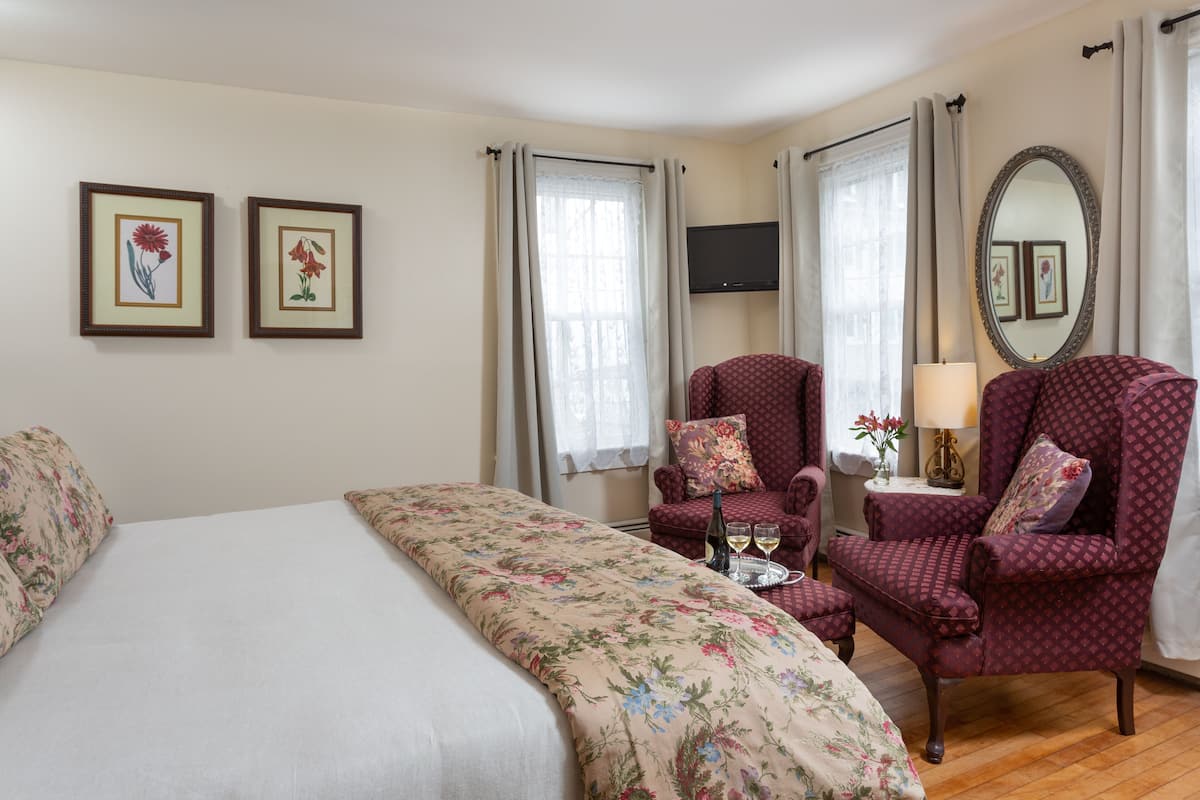 Une chambre d’hôtel avec un grand lit, deux fauteuils, une petite table avec une bouteille et des verres, et un téléviseur fixé au mur.